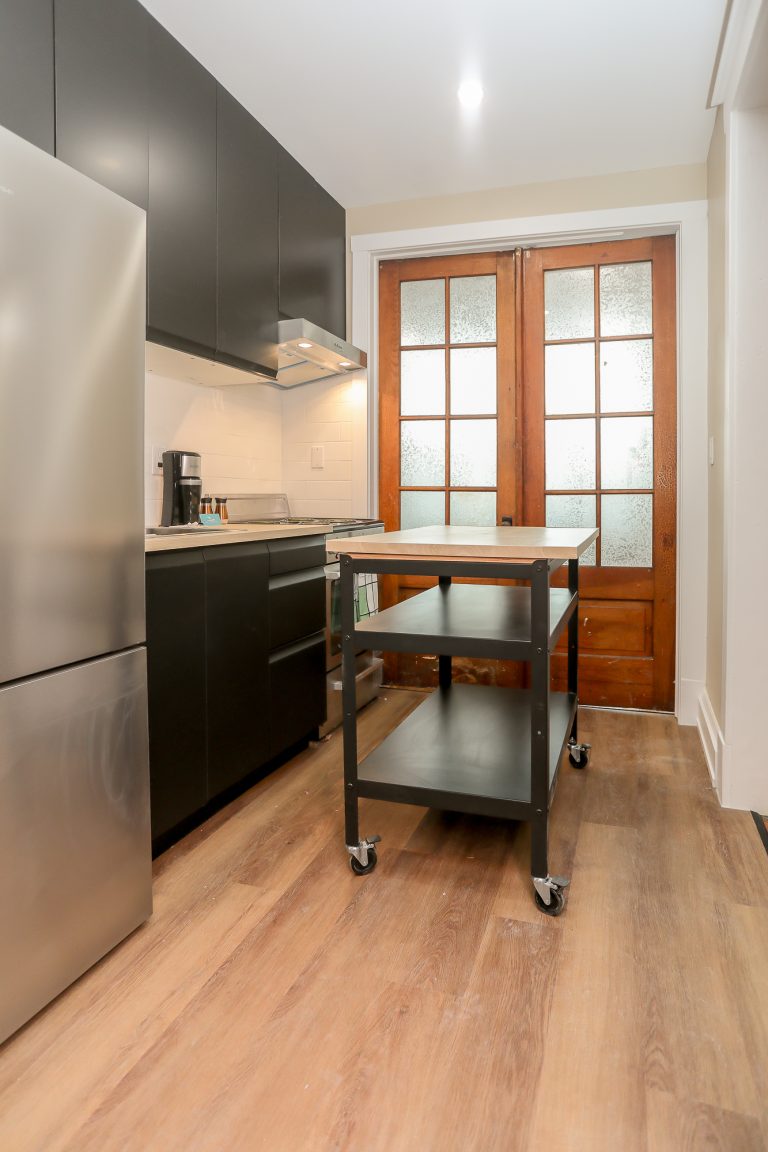 Modern kitchen with a black rolling portable kitchen island and natural wood french doors.