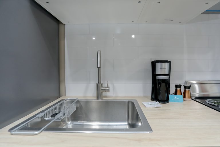 Apartment sink and faucet in front of a white tile backsplash.