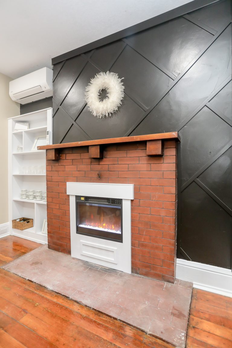 Red brick fireplace in front of black accent wall.