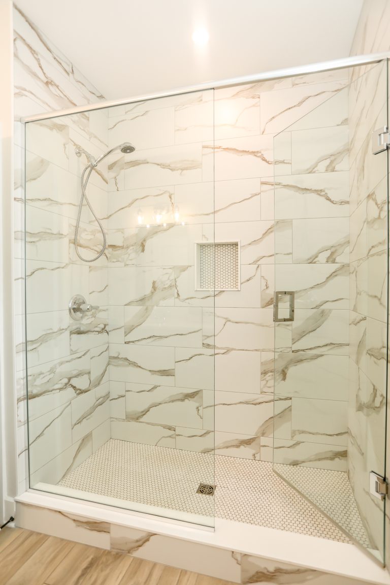 Marble tiled shower with clear glass doors.