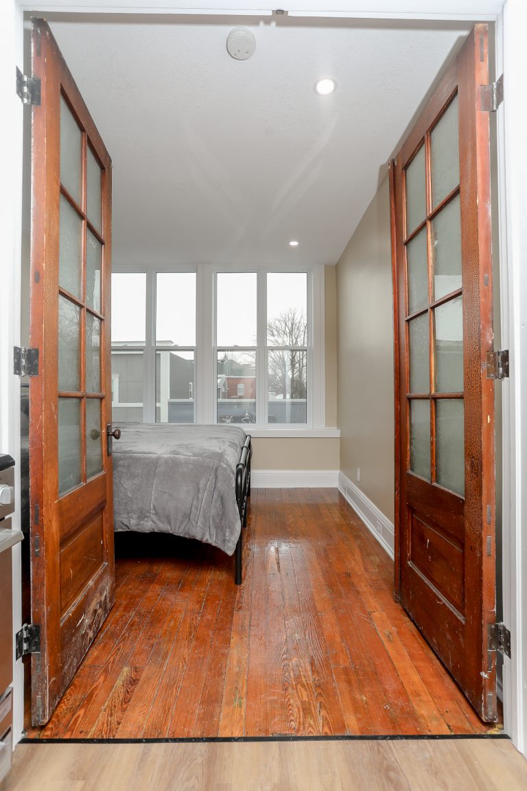 Master bedroom with plush grey bedspread and warm wooden floors.