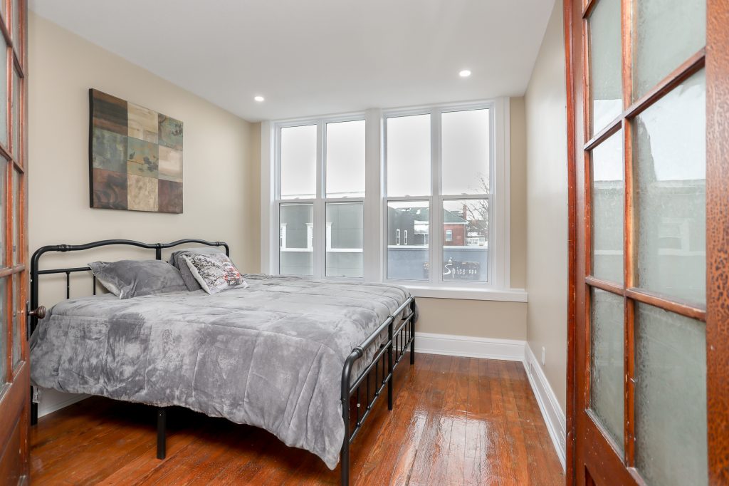 Master bedroom with plush grey bedspread and warm wooden floors.