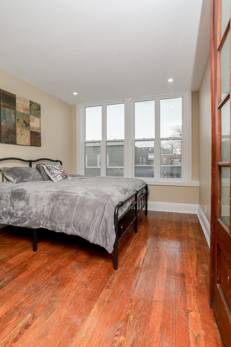 Master bedroom with plush grey bedspread and warm wooden floors.
