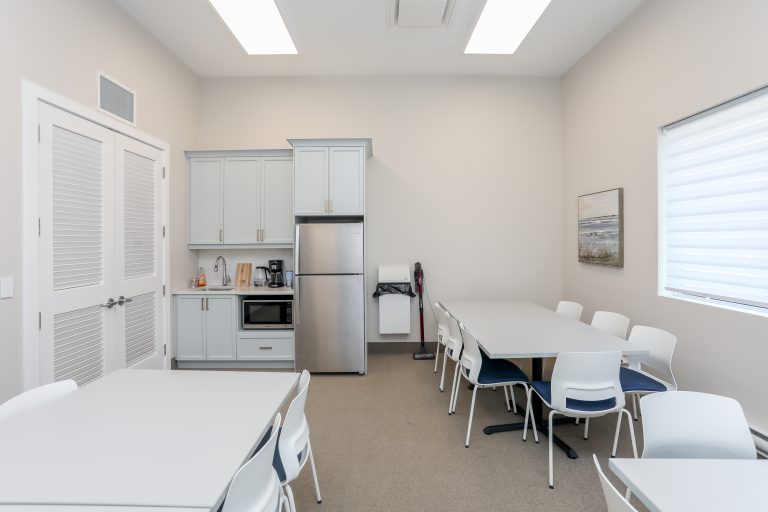White boardroom with kitchenette, chairs and tables.