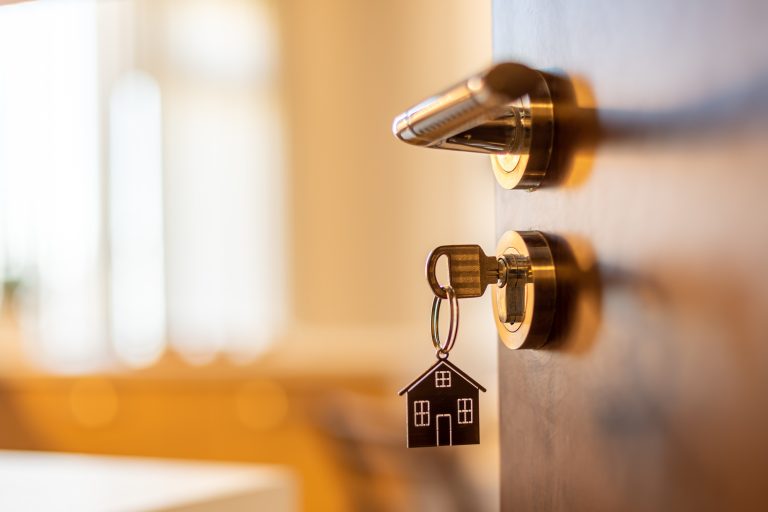 Open door to a new home. Door handle with key and home shaped keychain. Mortgage, investment, real estate, property and new home concept